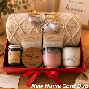 May include: A gift set in a red box containing a beige textured throw blanket tied with a grey ribbon and gold spoons, two Tea With Tae tea packets, a candle, a wooden coaster engraved with The Williams Family Est. 2024, and two ceramic cups.