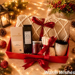 May include: A gift box containing a beige textured throw blanket tied with a red ribbon, a Moonstruck milk chocolate bar, a bag of Early Bird Blend coffee, a dark red candle in a glass jar, a white knit item, and a white ceramic mug with cracks.