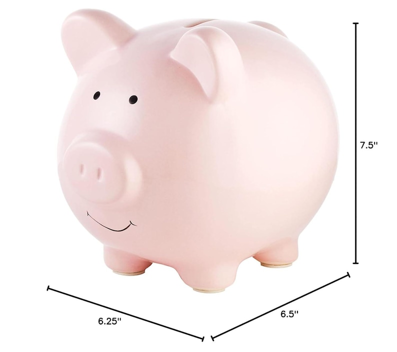 May include: A pink ceramic piggy bank with a smiling face and a small snout. It measures 7.5 inches tall, 6.25 inches wide, and 6.5 inches long.