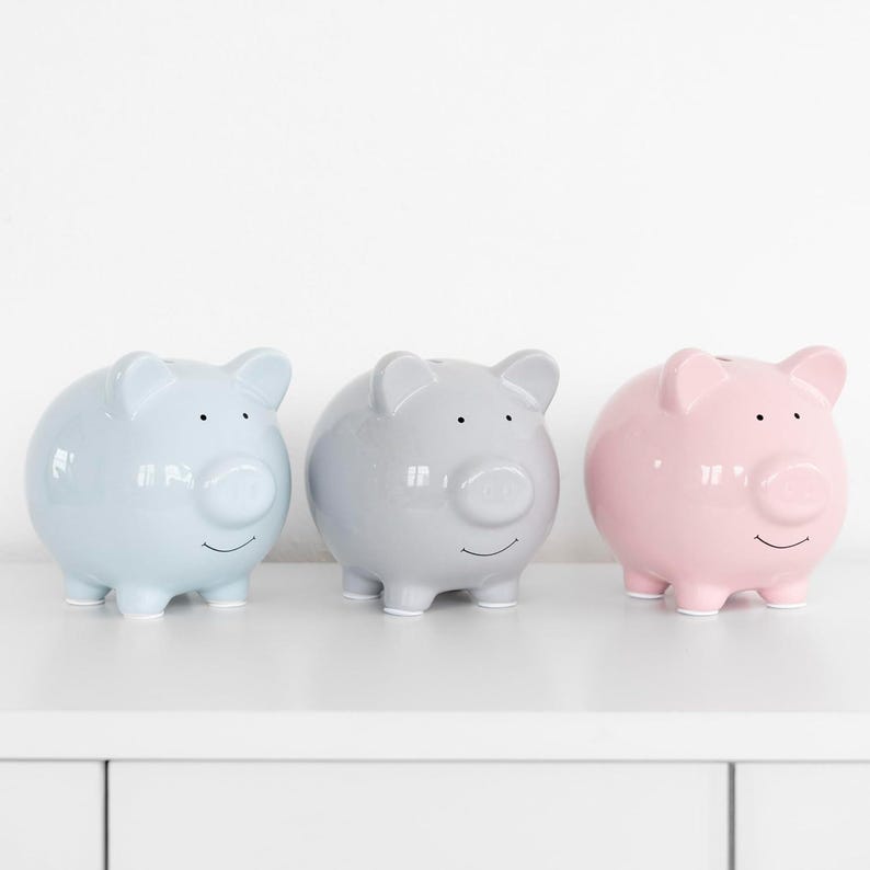 May include: Three ceramic piggy banks in different colors: light blue, gray, and pink. Each piggy bank has a simple, smiling face with black eyes and a snout.