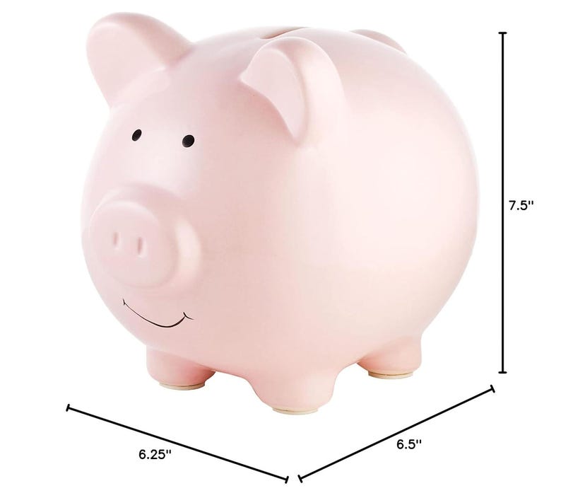 May include: A pink ceramic piggy bank with a smiling face and a small snout. It measures 7.5 inches tall, 6.25 inches wide, and 6.5 inches long.