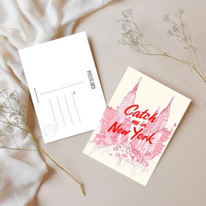 Könnte beinhalten: Zwei Postkarten. Eine zeigt eine rosa Illustration von New Yorker Gebäuden mit dem Text "Catch me in New York". Die andere ist leer mit dem Wort "POSTCARD" vertikal gedruckt.
