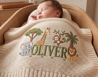 May include: A cream-colored knit baby blanket featuring an embroidered jungle theme with a gray elephant, a yellow giraffe, a brown monkey, and a lion. The name OLIVER is stitched in large green letters across the center of the blanket.