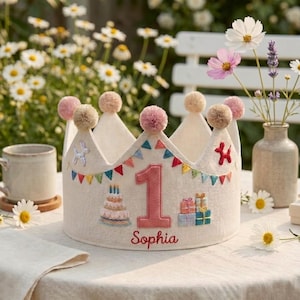 May include: A beige fabric crown featuring a large pink number one, embroidered birthday cake, gift boxes, and colourful bunting flags. The crown is topped with small pom-poms and includes the name Sophia embroidered in red script at the base.