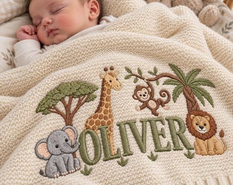 May include: A cream-colored knitted baby blanket featuring embroidered jungle animals including an elephant, a giraffe, a monkey, and a lion, with the name OLIVER stitched in large green letters across the center of the fabric.