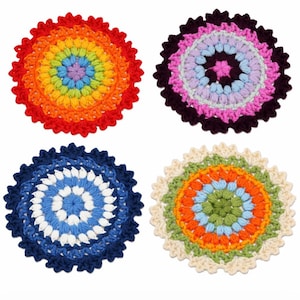 May include: Four colorful, crocheted coasters. One features a rainbow pattern, another has pink and purple hues, a third is blue and white, and the last has green, orange, and cream colors. Each coaster has a scalloped edge.