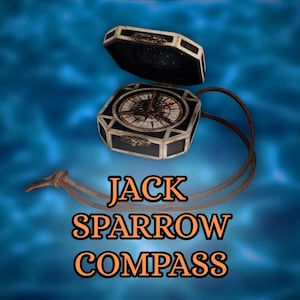Puede incluir: Una réplica de brújula con una caja negra y plateada, abierta para revelar una rosa de los vientos detallada. El texto "JACK SPARROW COMPASS" se muestra en letras naranjas debajo, con una correa de cuero marrón.