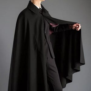 May include: A black cape with a wide collar and a matching suit. The cape is long and flowing, reaching the ankles. The suit includes a jacket, pants, and dress shoes. The outfit is all black, creating a sleek and formal appearance.