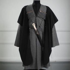 May include: A traditional gray and black outfit, likely a costume or historical garment. The ensemble includes a long gray tunic, a black cape, and a gray vest adorned with decorative elements. A decorative knife is attached to the vest.