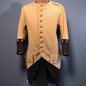 May include: A cream-coloured military-style jacket with gold buttons and black cuffs. The jacket has a high collar and two pockets with gold buttons. The bottom of the jacket has a black panel. The jacket is a historical garment.