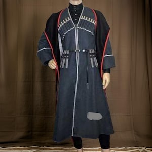 May include: A dark blue traditional coat with black accents and red trim. The coat features intricate white and silver embroidery along the front and sleeves. A black belt cinches the waist, and the coat is worn over a black turtleneck and leggings.