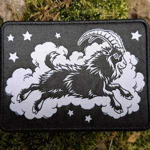 May include: Black rectangular patch featuring a white illustration of a goat leaping through clouds, surrounded by white stars. The goat has large curved horns and a detailed fur pattern. The patch has a black border.