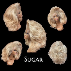 Può includere: Diverse parrucche bionde con uno stile ampio e cotonata, presentate su teste di manichino. Le parrucche presentano ricci voluminosi e un frontale in pizzo. La parola "SUGAR" è scritta in testo bianco. Lo sfondo è nero.