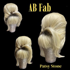 Op de afbeelding: Drie blonde pruiken op mannequinhoofden. De pruiken zijn gestyled in een klassieke updo met pony. De tekst "AB Fab" staat bovenaan en "Patsy Stone" onderaan. De achtergrond is zwart.