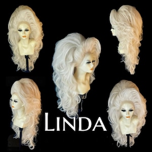 Puede incluir: Colección de cinco pelucas blancas peinadas en cabezas de maniquí. Las pelucas tienen cabello voluminoso y rizado, con rizos largos y sueltos. La palabra "LINDA" se muestra en texto blanco. El fondo es negro.