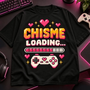 Könnte beinhalten: Ein schwarzes T-Shirt mit einer Pixel-Art-Grafik und dem Text CHISME LOADING. Das Design enthält einen rosa Ladebalken, einen weißen Gamecontroller sowie mehrere rosa Herzen und gelbe Sterne, die um den Text und die Grafiken angeordnet sind.