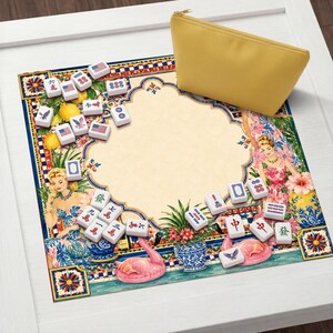 Pode incluir: Uma bolsa amarela com z&iacute;per repousa sobre um tapete decorativo para o jogo de Mahjong. O tapete apresenta um design vintage com ilustra&ccedil;&otilde;es de mulheres, flamingos e padr&otilde;es florais. As pe&ccedil;as de Mahjong est&atilde;o espalhadas.