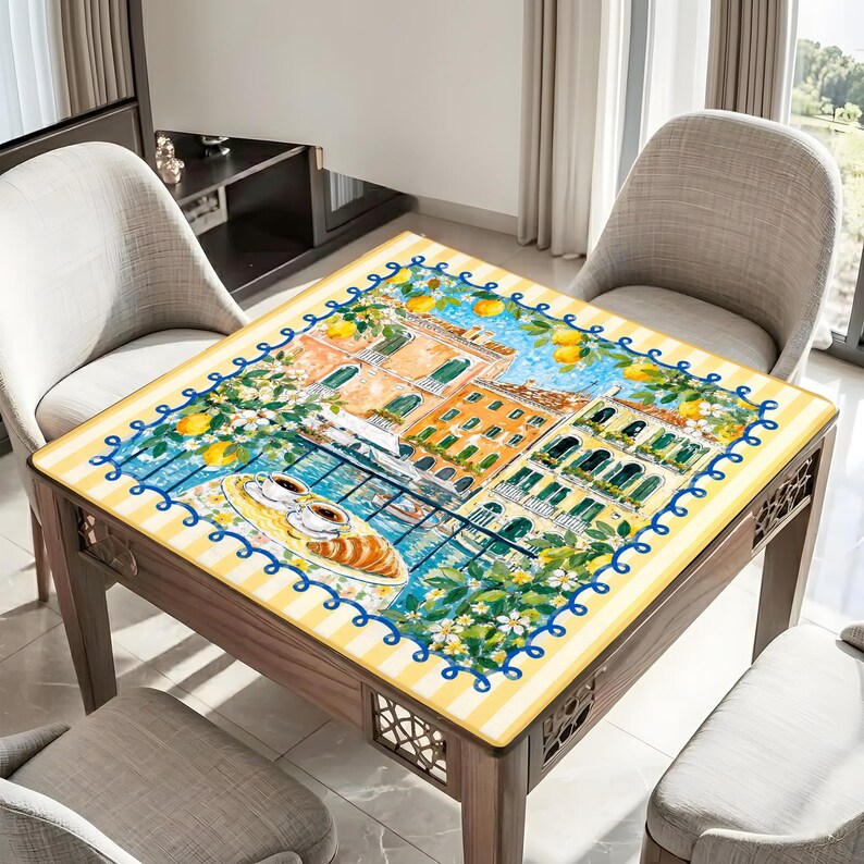 May include: Square wooden table with a glass top depicting an Italian cityscape. The table has a yellow and white striped border with a blue wavy trim. The table is surrounded by three grey chairs. The table's dimensions are in centimetres.