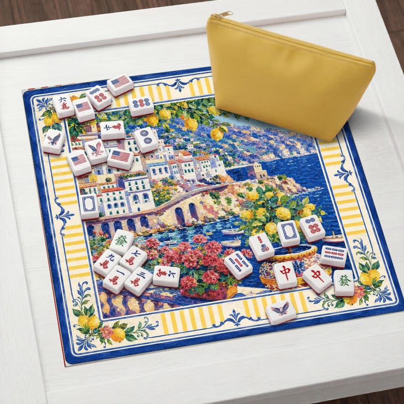 Puede incluir: Un juego de Mahjong con fichas con dise&ntilde;os de banderas americanas y otros s&iacute;mbolos, esparcidas sobre una alfombra decorativa con una escena costera. Una bolsa amarilla con cremallera est&aacute; cerca. La alfombra tiene un borde azul y amarillo.