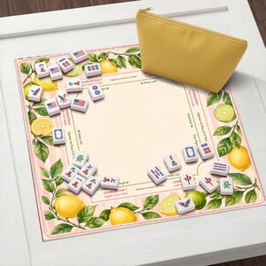May include: A Mahjong game set with tiles, a game board, and a yellow zippered pouch. The board features a pink and white striped background with lemon and leaf illustrations. The tiles have various symbols and designs.