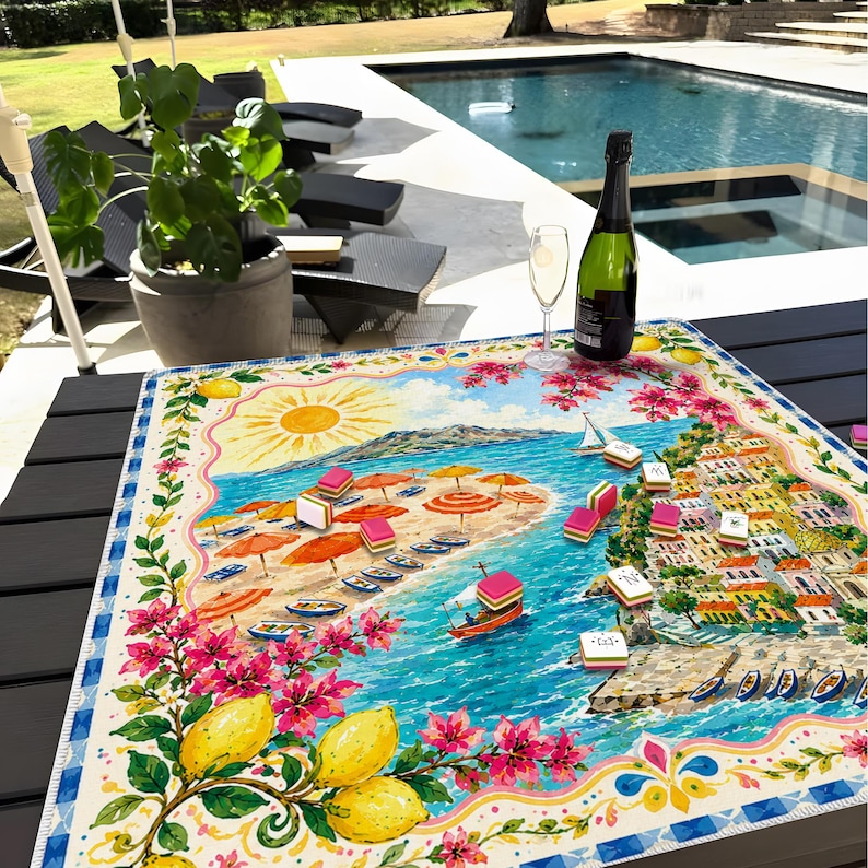 Puede incluir: Un mantel colorido con tem&aacute;tica de playa, con una vibrante ilustraci&oacute;n de una escena de playa soleada, completa con sombrillas, botes y un pueblo costero. El mantel est&aacute; decorado con limones y flores, y una botella de champ&aacute;n y dos copas encima.