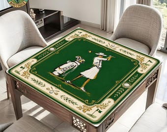 May include: A square table cover featuring a dark green center with a graphic of a golfer and a golf bag. The border is cream-colored with gold-toned filigree, golf clubs, and golf balls. The design includes small green flags and golf motifs.