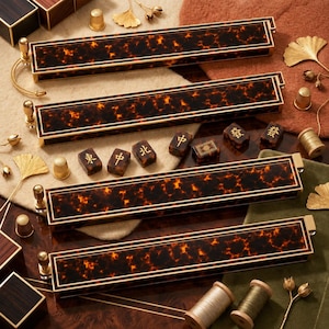 May include: Four rectangular mahjong racks featuring a dark brown and orange tortoiseshell pattern with gold-toned metal trim and end caps. Six small mahjong tiles with gold-colored Chinese characters are arranged between the racks.