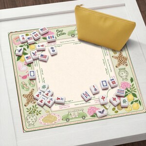 Pu&ograve; includere: Un astuccio giallo con cerniera &egrave; appoggiato su un tappetino decorativo per il gioco del Mahjong. Il tappetino presenta un design floreale e a tema alimentare con le parole "Ciao Bella" e varie tessere del Mahjong. Le tessere del gioco sono bianche con segni rossi e blu.