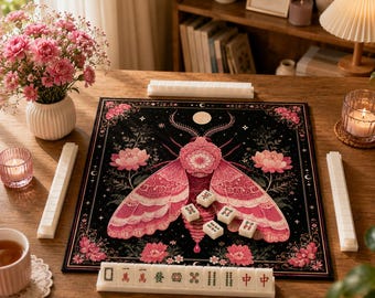 Puede incluir: Un tapete de mahjong cuadrado con una gran ilustración de una polilla rosa sobre un fondo negro con detalles florales, rodeado por cuatro soportes blancos y varias fichas de mahjong con caracteres y símbolos chinos sobre el tapete.