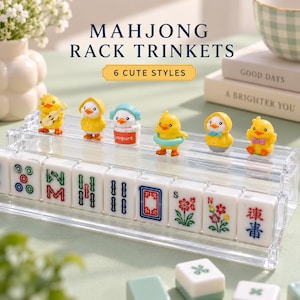 Könnte beinhalten: Ein durchsichtiger Acryl-Mahjong-Ständer mit acht weißen Mahjong-Steinen mit bunten Symbolen und sechs kleinen gelben Entenfiguren. Der Text "MAHJONG RACK TRINKETS" und "6 CUTE STYLES" ist über dem Ständer aufgedruckt. Die Figuren haben verschiedene Accessoires.