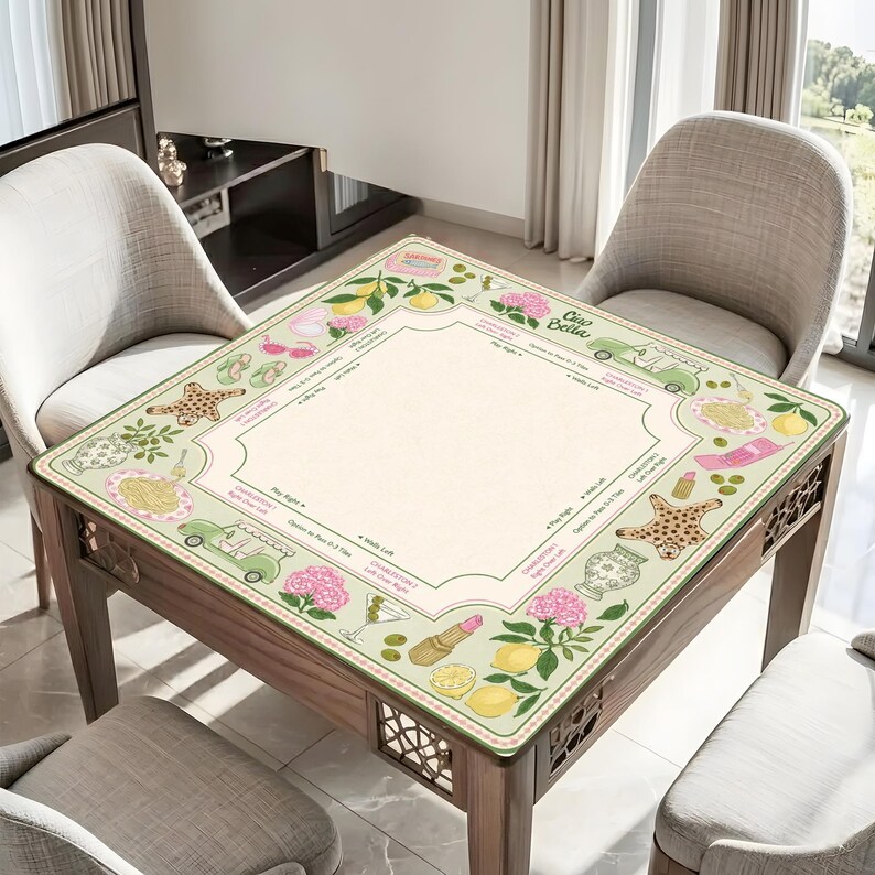 Pu&ograve; includere: Un tavolo quadrato in legno con un piano decorativo con un bordo verde chiaro con illustrazioni di limoni, fiori e altri oggetti. Il tavolo ha un centro beige chiaro ed &egrave; circondato da due sedie.