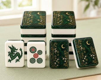 May include: A set of mahjong tiles featuring two stacks of dark green tiles with gold bamboo and crescent moon designs. Two individual tiles stand in front, one displaying a green dragon illustration and the other showing five circular patterns.