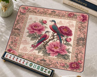 May include: A rectangular mahjong mat featuring a pink border with floral and pagoda motifs, surrounding a central illustration of two birds perched on a branch amidst large pink peonies. A mahjong tile rack and a white pen are included.