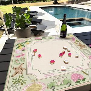 Pu&ograve; includere: Un tappetino da gioco beige con dettagli rosa e verdi, con illustrazioni di limoni, scarpe e un'auto da golf. Il tappetino ha una griglia per giocare con tessere rosse e bianche. Una bottiglia di champagne e un bicchiere sono sul tavolo.