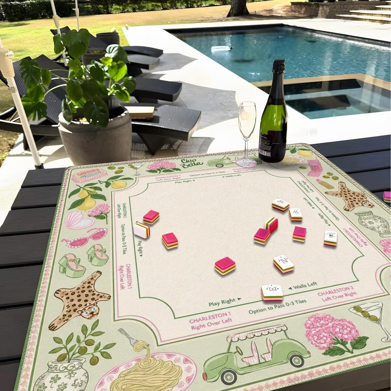 Pu&ograve; includere: Un tappetino da gioco beige con dettagli rosa e verdi, con illustrazioni di limoni, scarpe e un'auto da golf. Il tappetino ha una griglia per giocare con tessere rosse e bianche. Una bottiglia di champagne e un bicchiere sono sul tavolo.