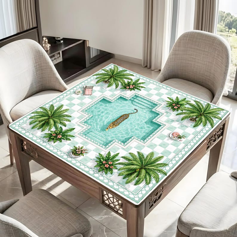 May include: A square table featuring a printed tablecloth with a light blue and white checkered pattern. The design depicts a swimming pool with a leopard swimming in the center, surrounded by green palm trees and small floral accents.