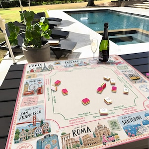May include: A travel-themed board game with a beige playing surface featuring illustrations of famous landmarks like the Eiffel Tower and the London Eye. Pink and white game pieces are scattered across the board, with a bottle of champagne and a glass nearby.