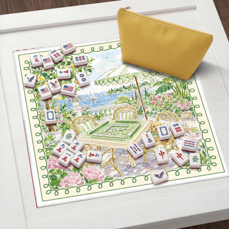 May include: A yellow zippered pouch rests on a Mahjong game mat with a scenic illustration. The mat features a table set for play, surrounded by tiles with various symbols and numbers. The scene includes a coastal view with a parasol and floral accents.
