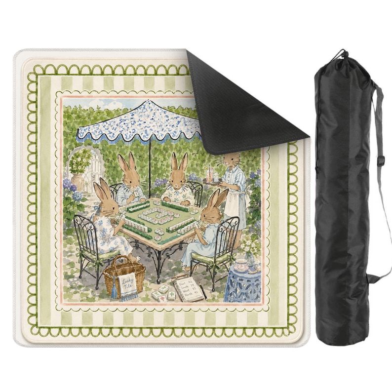 May include: A square outdoor blanket featuring a watercolor illustration of four rabbits playing mahjong under a blue and white umbrella, with a light green striped border and a scalloped edge. Includes a black cylindrical carrying bag with a strap.