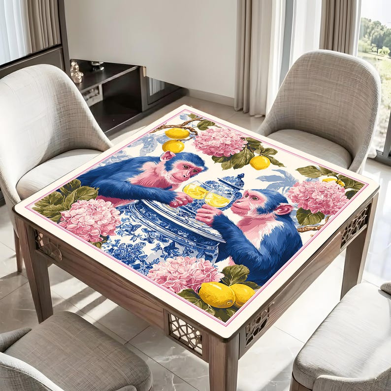 Pu&ograve; includere: Tavolo quadrato in legno con piano decorativo raffigurante un'illustrazione stravagante di due scimmie blu. Le scimmie interagiscono con un pezzo di porcellana blu e bianca, circondato da fiori rosa e limoni. Il tavolo ha una finitura in legno chiaro.