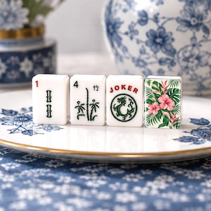 May include: Four rectangular white Mahjong tiles arranged in a row. The first tile shows a red number 1 and green bamboo symbols. The second shows a black number 4 and bamboo. The third features a red JOKER and a green dragon. The fourth has pink flowers.