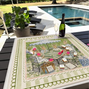 May include: A square fabric game mat featuring a printed illustration of rabbits playing mahjong under a parasol. The mat has a light green scalloped border and includes scattered mahjong tiles, a woven basket labeled Lucky Tile, and a book.