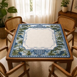 May include: A square wooden table with a decorative mat featuring a tropical landscape design in blue and white. The mat has a central cream-colored area with text, surrounded by palm trees and ocean scenes. Four wooden chairs surround the table.