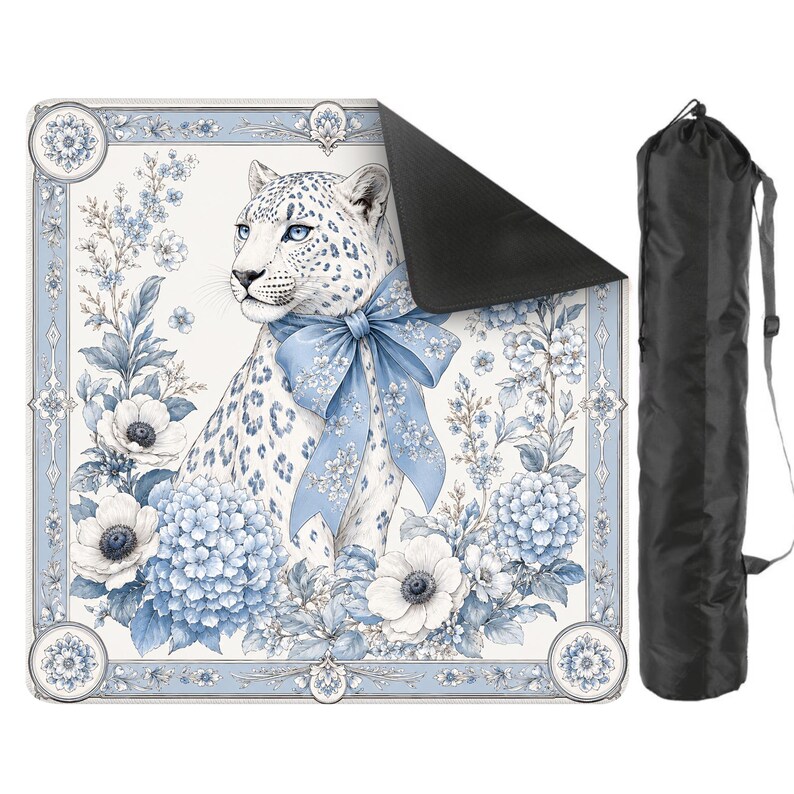 May include: A square mat featuring a white leopard with blue spots and a large blue bow around its neck, surrounded by blue and white floral illustrations. The mat has a black underside and comes with a black cylindrical carrying bag with a strap.