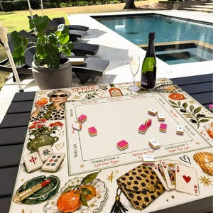 Puede incluir: Un tapete de Mahjong cuadrado con un dise&ntilde;o impreso de una mujer con gafas de sol, una botella de Aperol, cartas de juego, un bolso de leopardo y naranjas. El tapete incluye etiquetas de texto para las reglas de Charleston y direcciones de juego.