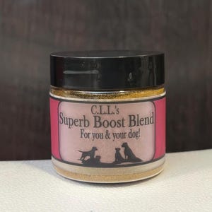 May include: A small glass jar with a black lid, filled with a golden powder. The jar has a pink label with the text "C.L.L.'s Superb Boost Blend For you & your dog!" and silhouettes of dogs.