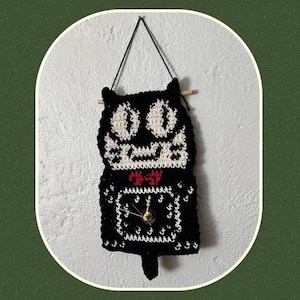 May include: A black and white crochet cat clock hanging on a wall. The clock features a cat face design with a red bow tie and a clock face with gold hands. The text "Cat Clock crochet pattern" is displayed below the clock.