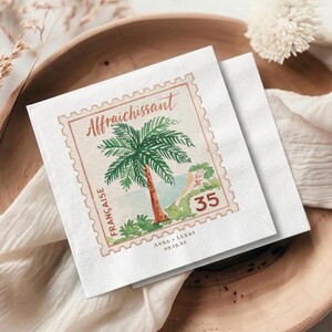 May include: A square white paper napkin featuring a postage stamp design with a watercolor palm tree, the text Affraichissant, Française, and 35, along with the personalized text Anna + Lukas and the date 09.19.XX printed in a dark brown font.