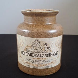 Può includere: Un barattolo di senape vintage con tappo in sughero. Il barattolo marrone ha un'etichetta con illustrazioni e testo in francese. L'etichetta recita "Moutarde à l'Ancienne" e "Armand Bizouard".