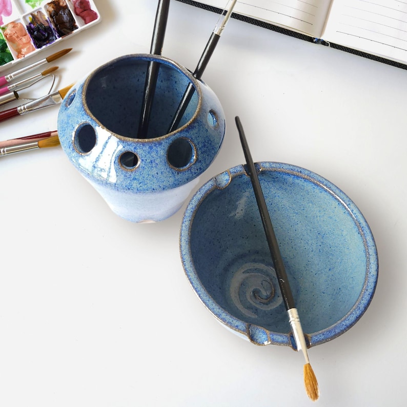 May include: A blue ceramic brush holder with multiple holes for brushes and a matching blue ceramic bowl. The bowl has a swirl design and is perfect for rinsing brushes.